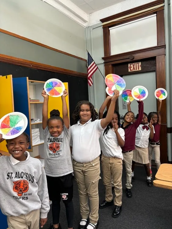 St. Aloysius students proudly holding up their colorful art projects in the classroom